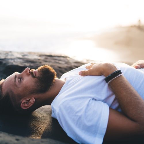 Bearded man with closed eyes lysing and resting during pastime for pranayama breathing in nature environment, calm male yogi feeling mindfulness enlightenment during holistic healing and retreat