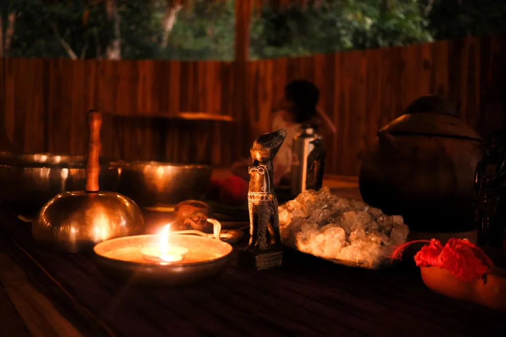 Healing tools, including sage, a singing bowl, and crystals used in somatic healing retreats, illuminated by firelight.